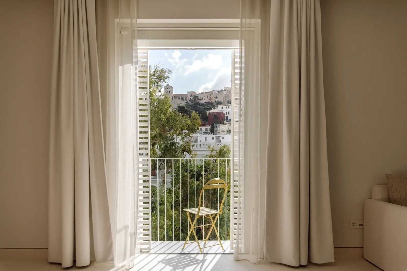 Blick vom Balkon durch Vorhänge auf die historische Altstadt auf dem Hügel.