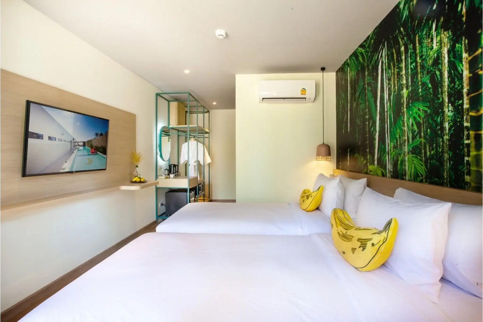 Hell eingerichtetes Hotelzimmer mit zwei Betten, Wand-TV und Klimaanlage.