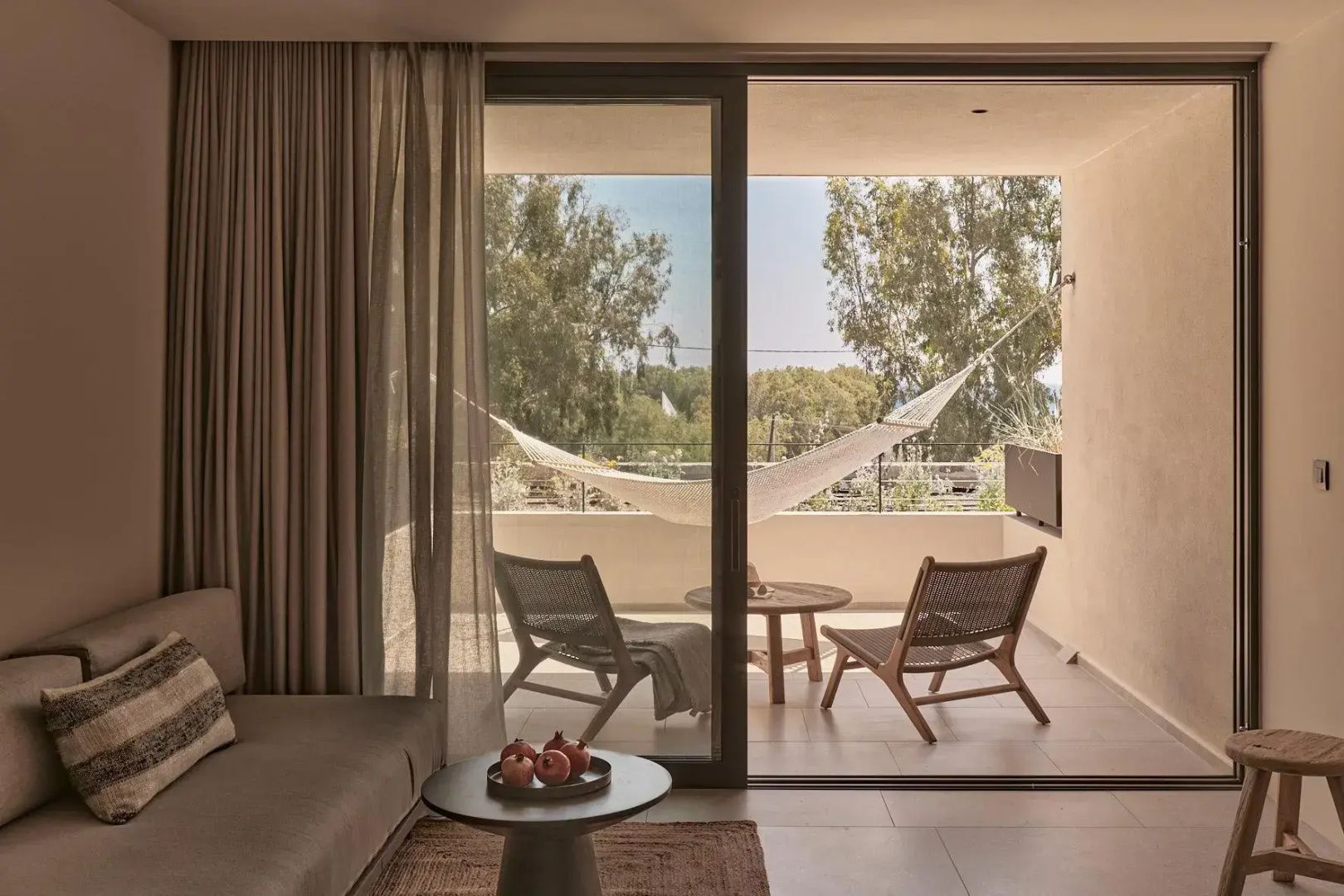 Blick durch die Fenstertür auf einen Balkon mit zwei Holzstühlen, Tisch und Hängematte.