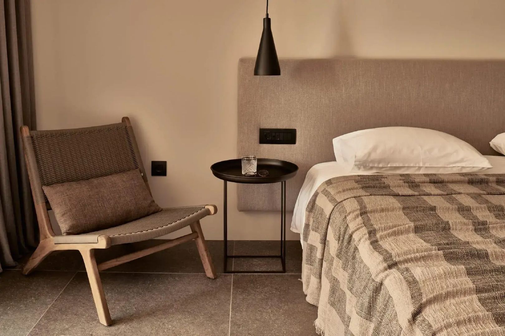 Ecke eines Hotelzimmers mit einem Bett, einem Sessel aus Holz und einem kleinen runden Beistelltisch.