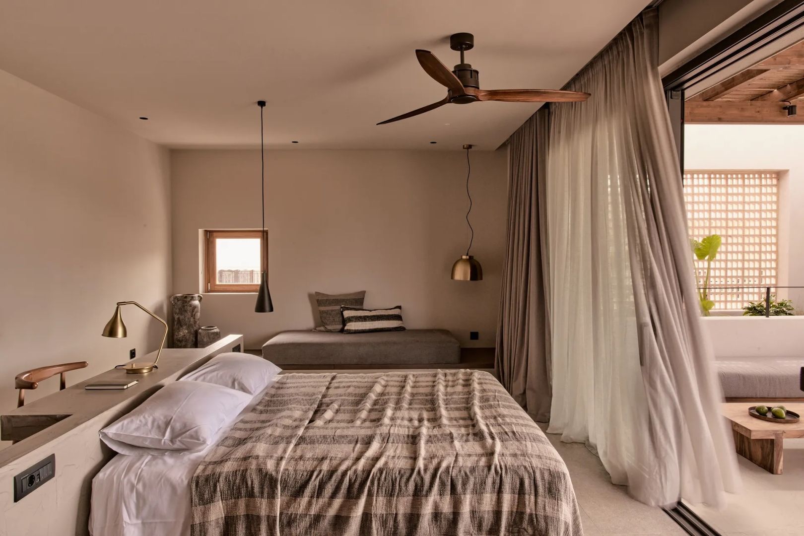 Schlafbereich mit Doppelbett, Sitzgelegenheit an der Wand und Deckenventilator.
