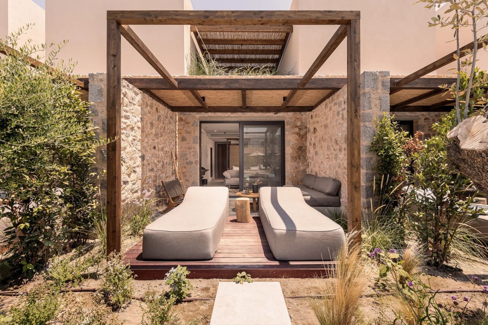 Terrasse einer Suite mit zwei Liegen unter einem Pavillon und Natursteinwänden.