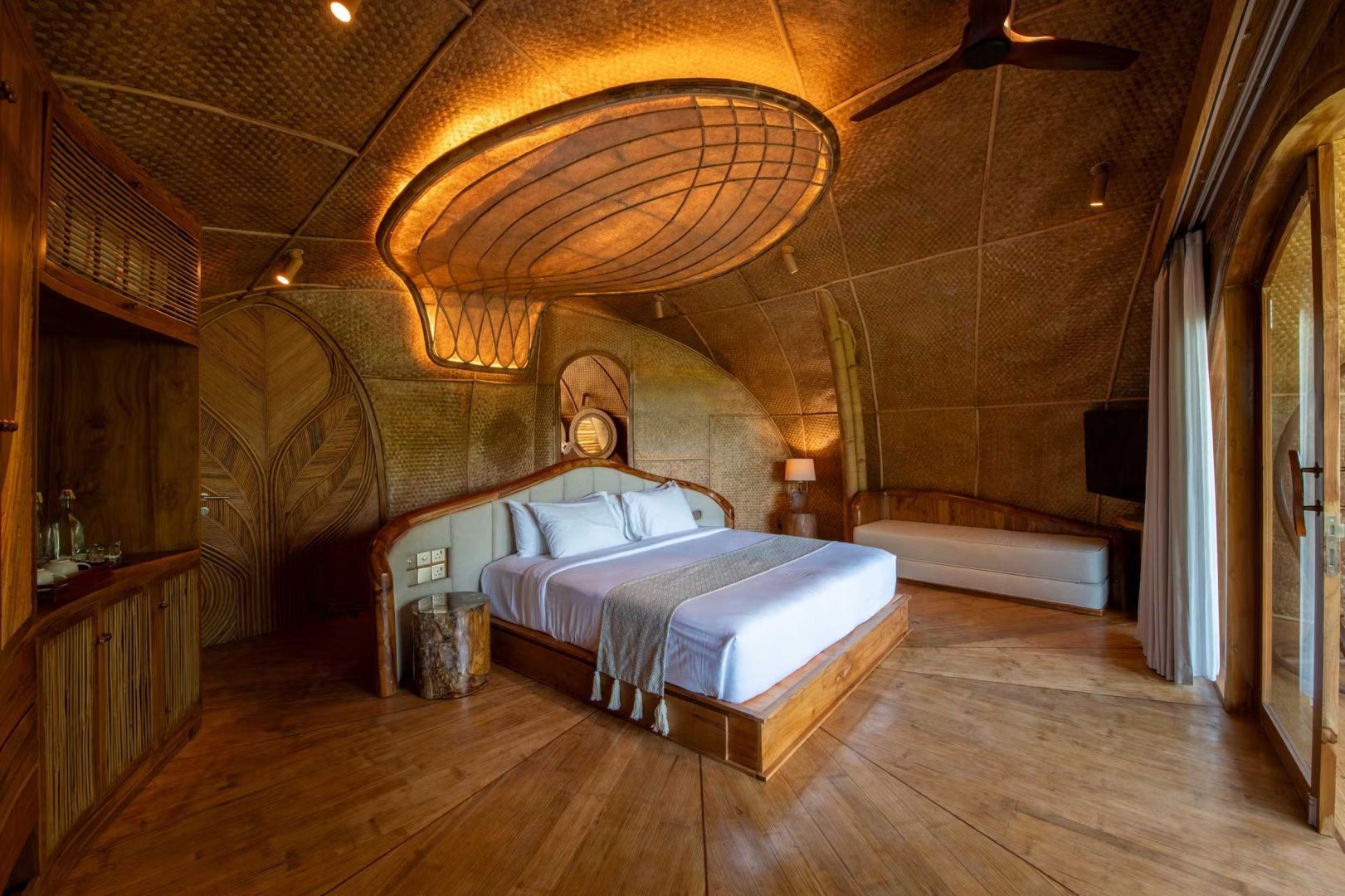 Geräumiges Schlafzimmer aus Bambus mit Holzfußboden, großem Doppelbett und beleuchtetem Deckenelement.
