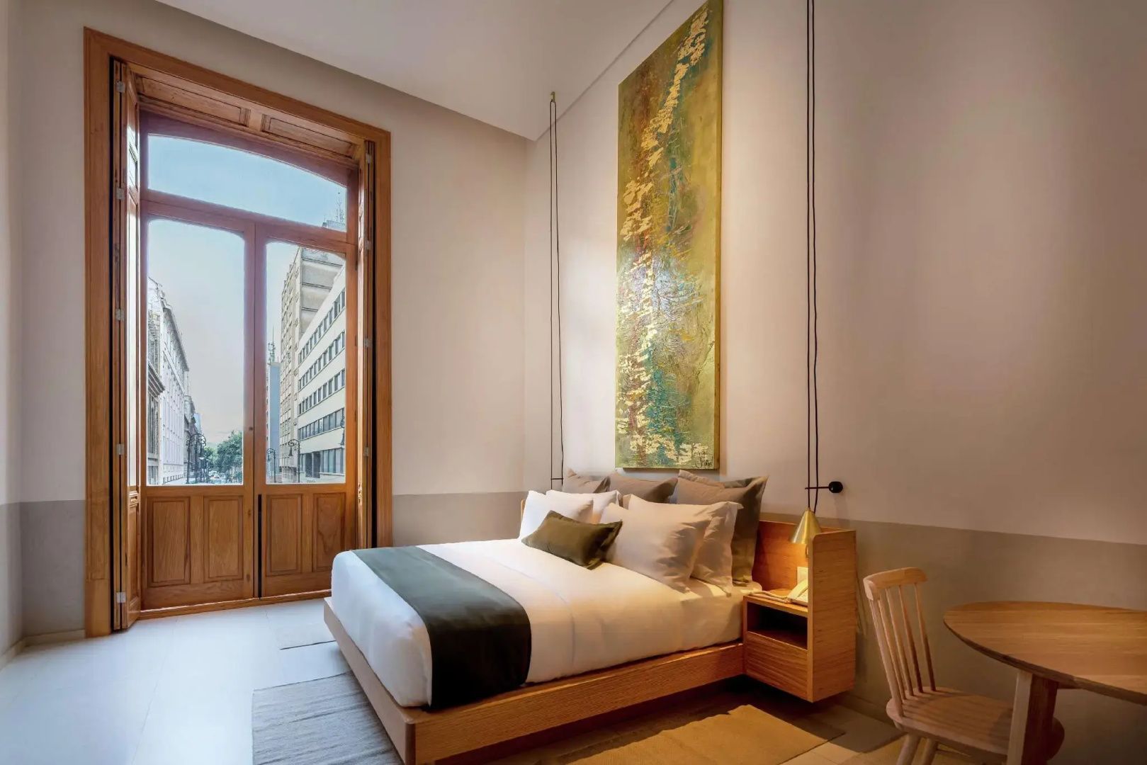 Modernes Schlafzimmer mit hohem Bett, langem Wandbild und Holztüren zum Balkon.
