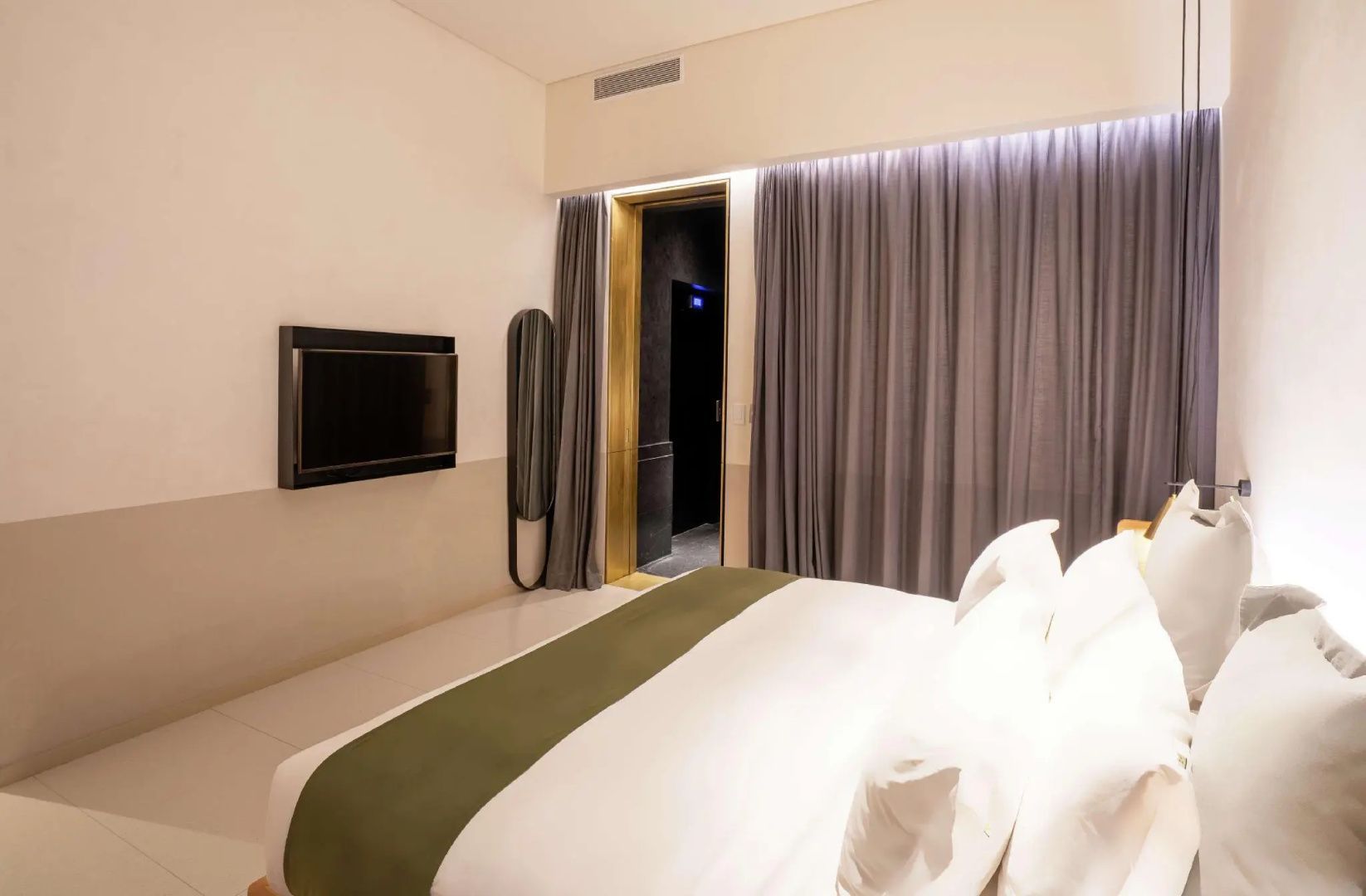 Hotelzimmer mit an der Wand montiertem Fernseher, grauem Vorhang und Durchgang.