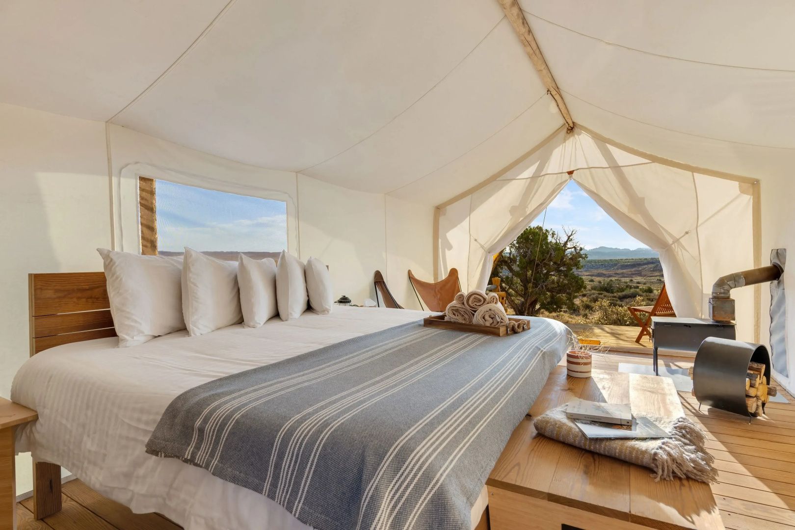 Blick aus einem geöffneten Zelt mit Doppelbett auf die umliegende Landschaft.