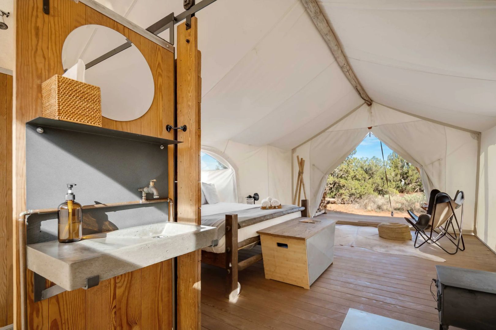 Innenbereich eines Glampingzelts mit Waschbecken und Bett auf Holzboden.