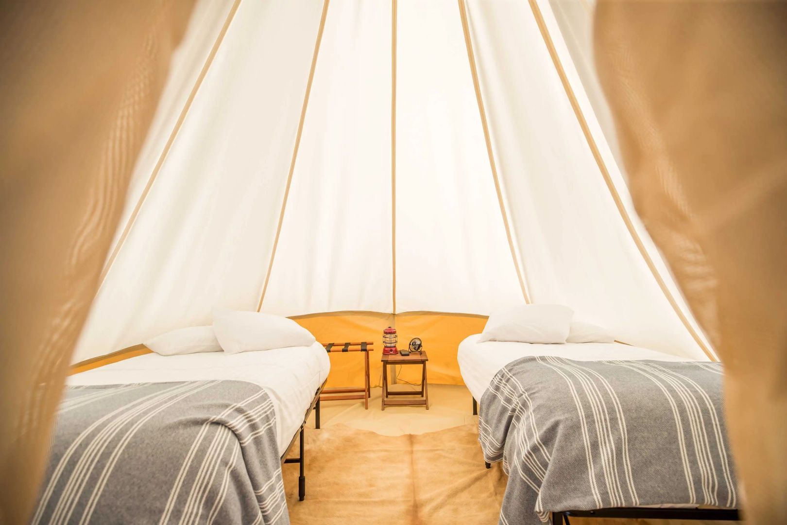 Zweibettzimmer in einem Tipi-Zelt mit Holzfußboden und kleiner Nachtkonsole.