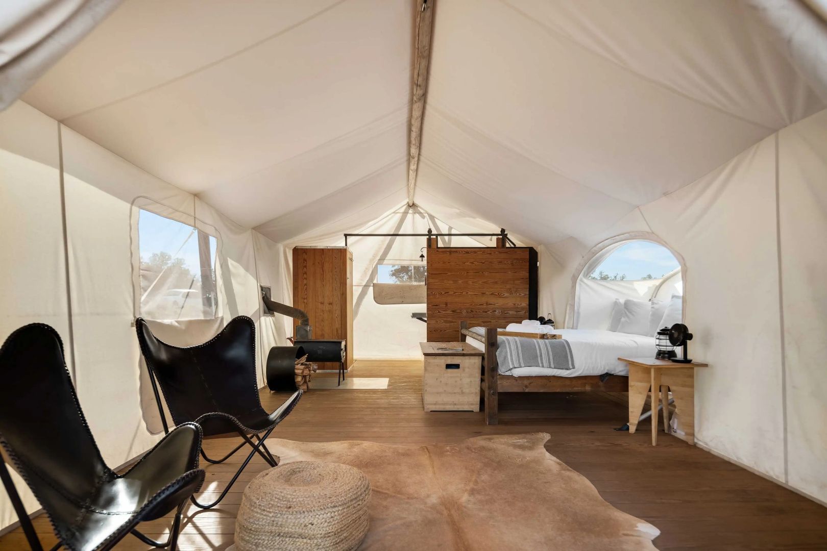 Geräumiges Glampingzelt mit Sitzbereich, Holzofen und großem Bett.