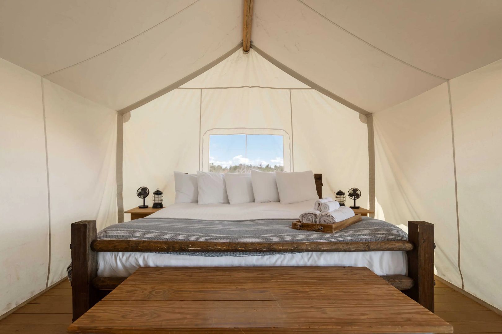 Großes Doppelbett mit Holzrahmen und weißen Kissen in einem hellen Safarizelt.