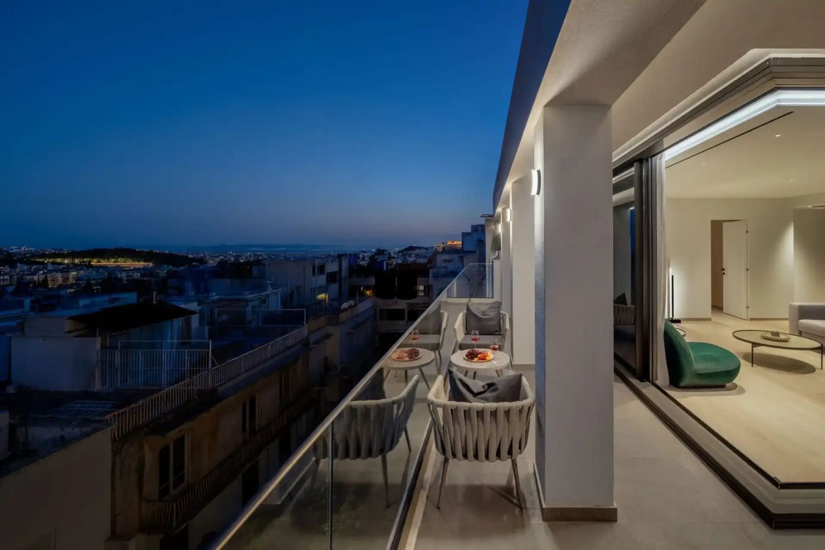 Balkon mit Sesseln und kleinen Tischen bei Abenddämmerung mit Blick über die Dächer.