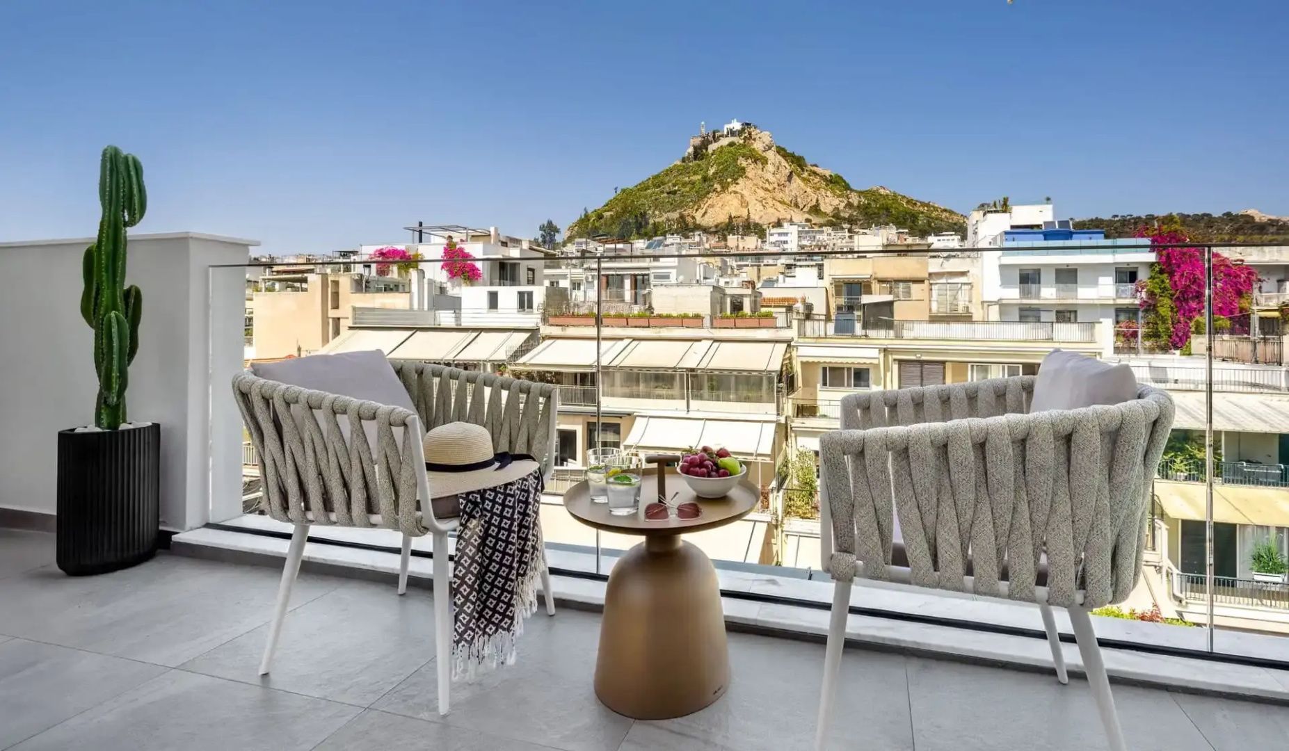Balkon mit zwei Sesseln und Tisch mit freiem Blick auf die Stadt und einen Hügel.