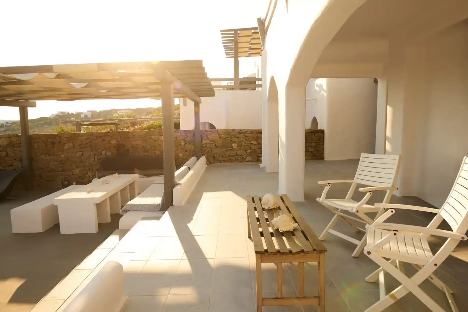 Sonnendurchflutete Terrasse mit Sitzgelegenheiten aus Holz und weiß gekalkten Wänden.