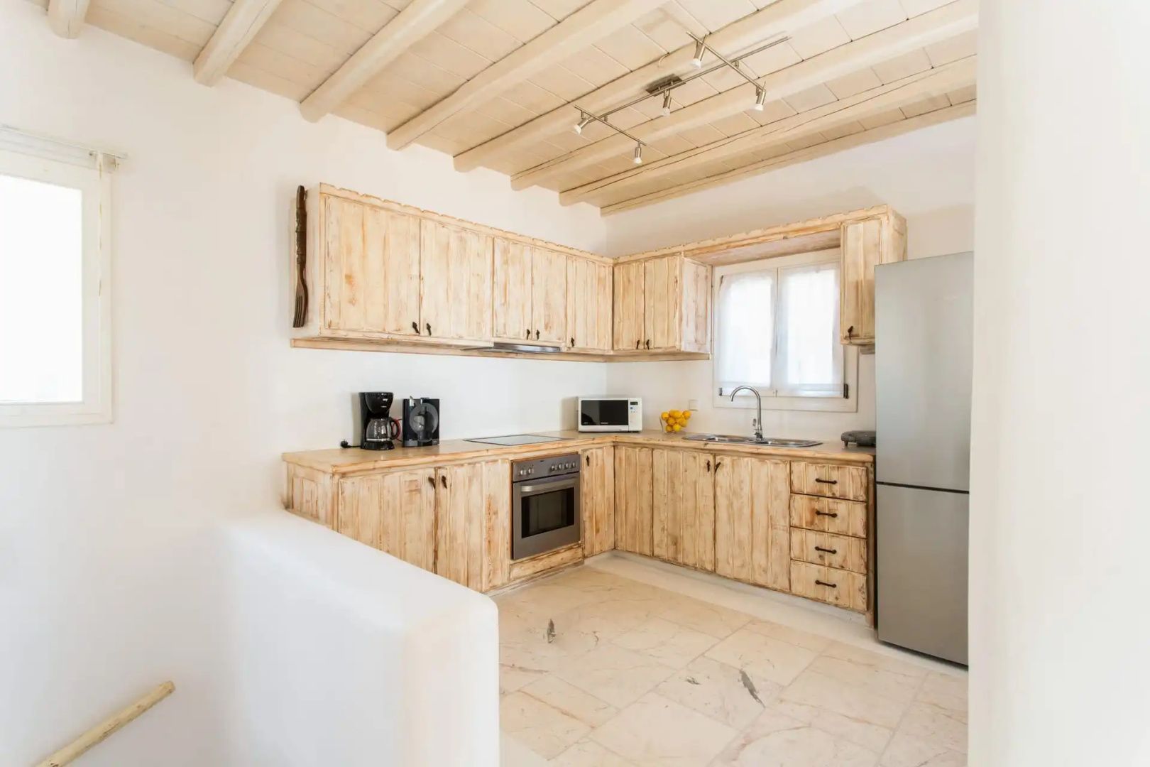 Voll ausgestattete Küche mit hellen Holzschränken, modernem Kühlschrank und Holzbalkendecke.