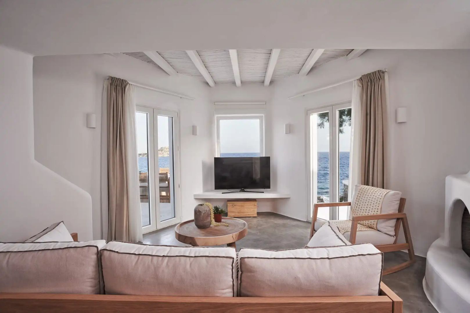 Heller Wohnbereich mit Sofa, Couchtisch und Fenstern mit Ausblick auf das Meer.