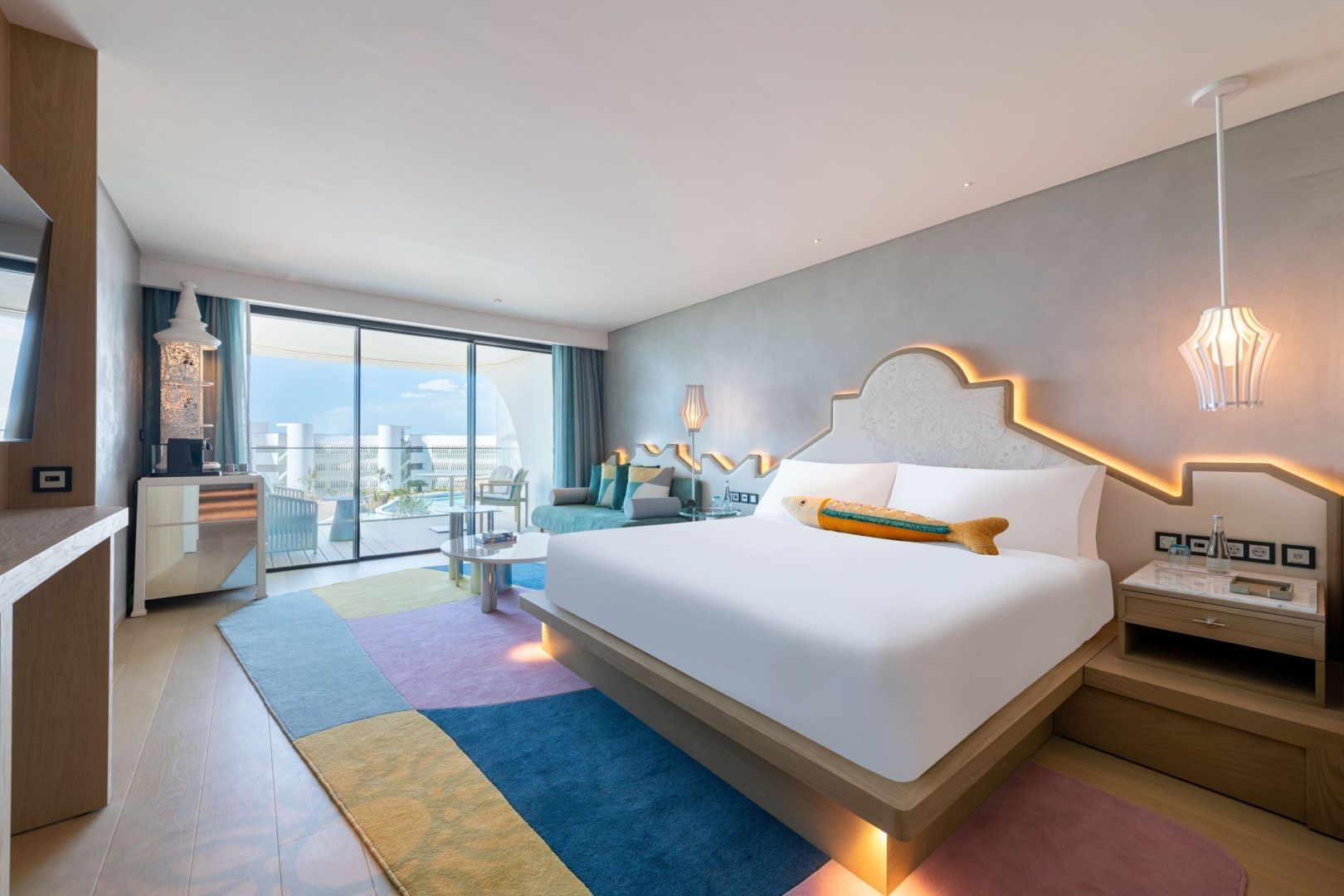 Modernes Hotelzimmer mit Doppelbett, buntem Teppich und Balkonzugang.