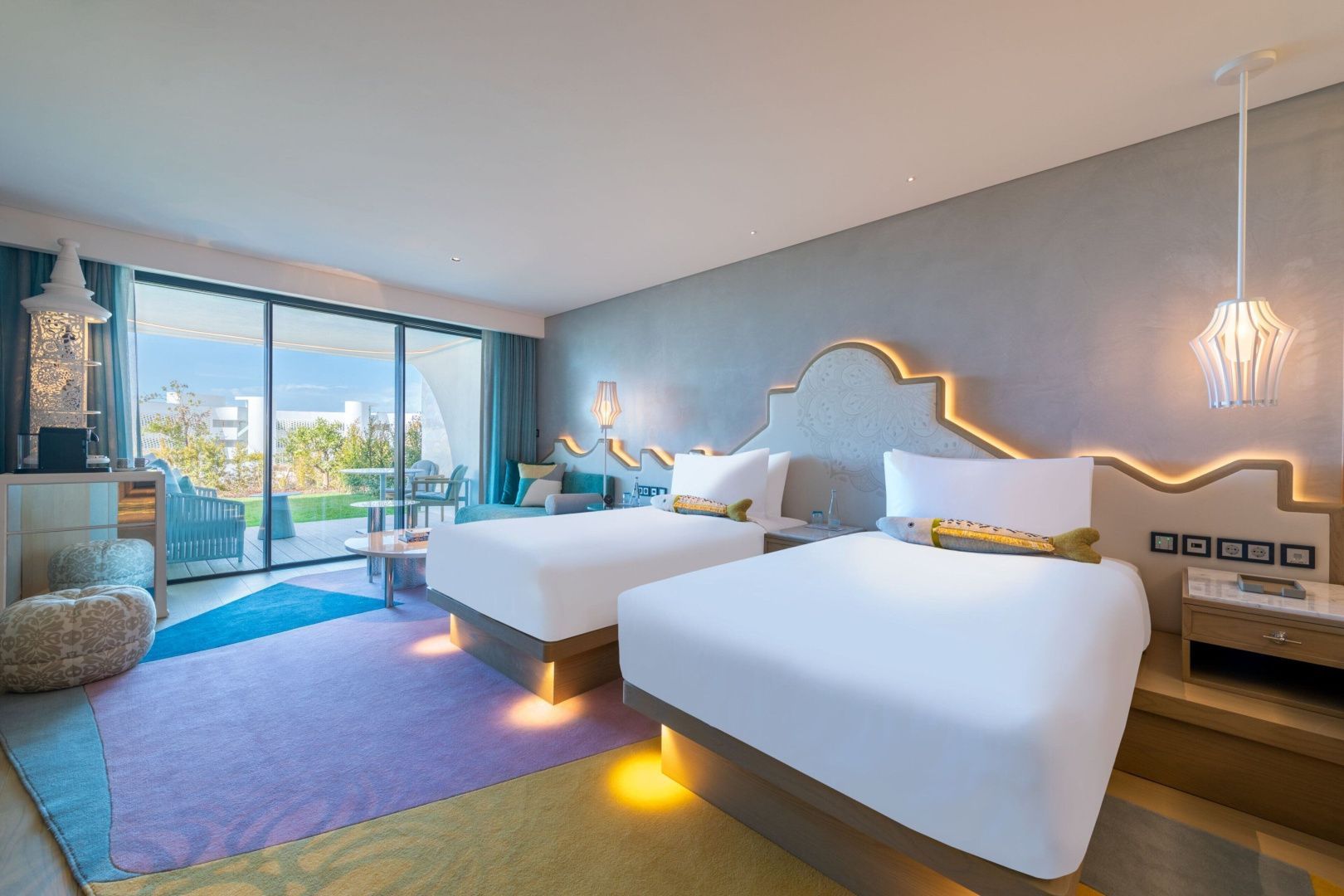 Modernes Hotelzimmer mit zwei Einzelbetten, farbigem Teppich und Balkonzugang.