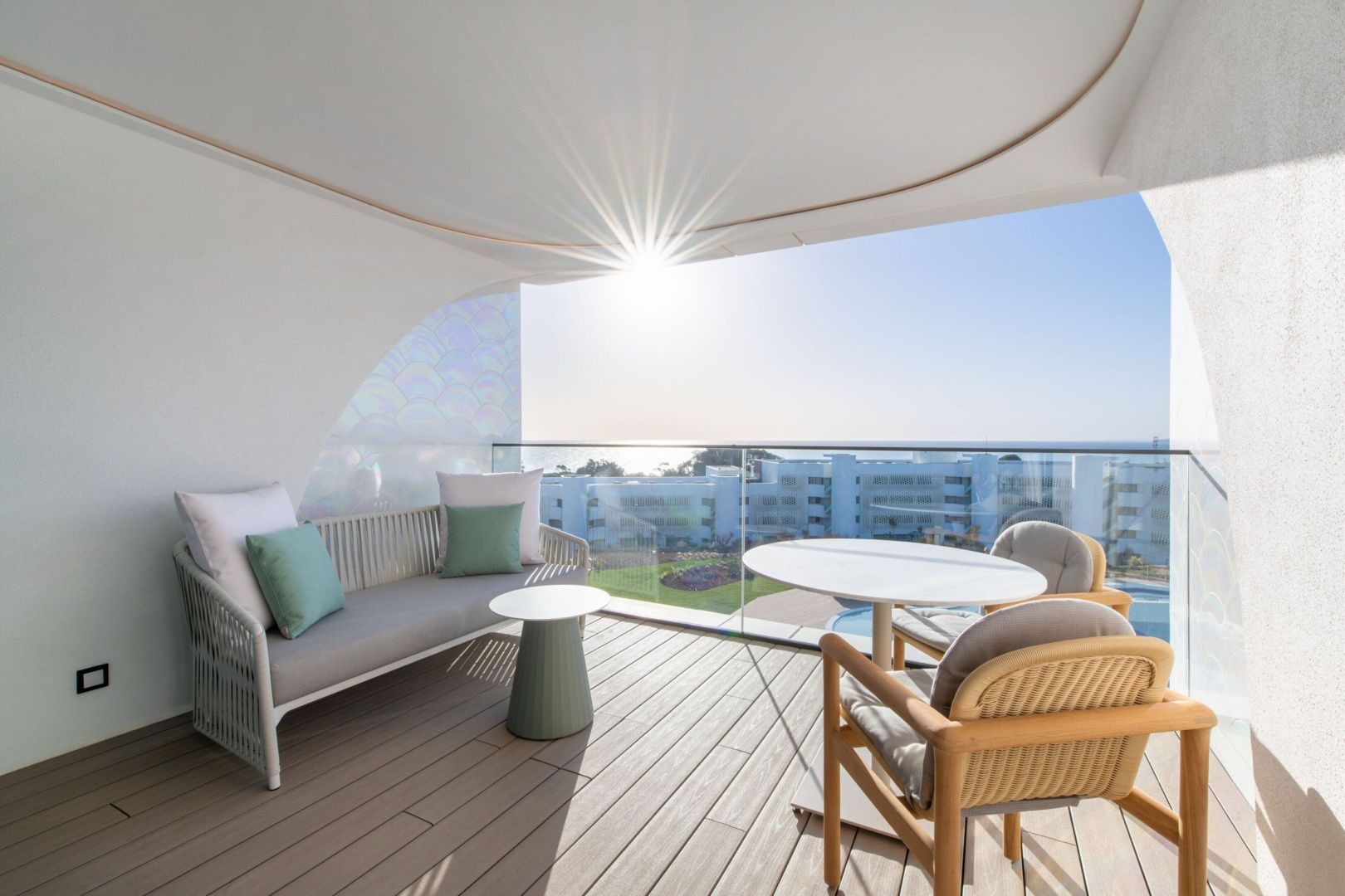 Sonnige Terrasse mit Couch, Tisch, Stühlen und Ausblick auf die Anlage.