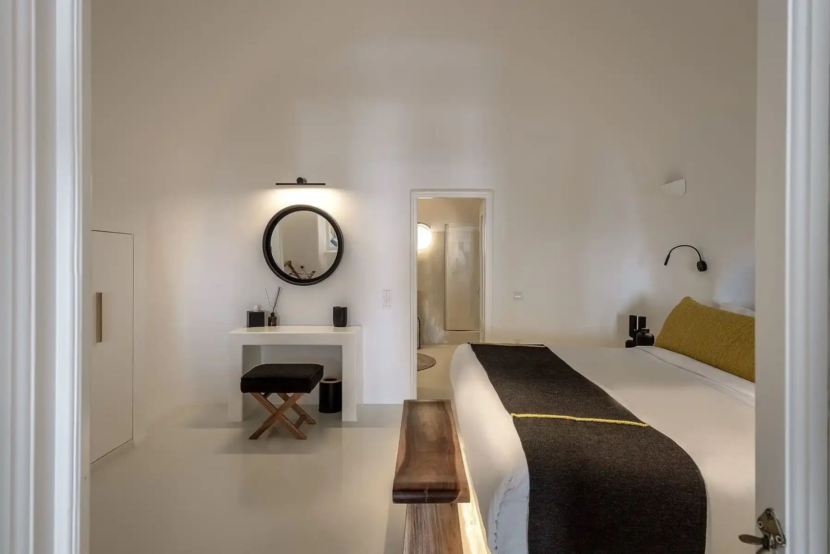 Weiß eingerichtetes Schlafzimmer mit Doppelbett, Frisiertisch und rundem Wandspiegel.