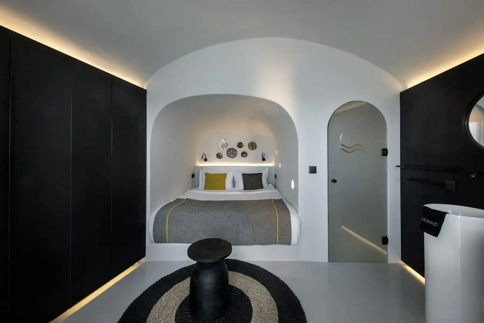 Weißes Höhlenschlafzimmer mit in eine Nische gebautem Doppelbett und runden Teppichen.
