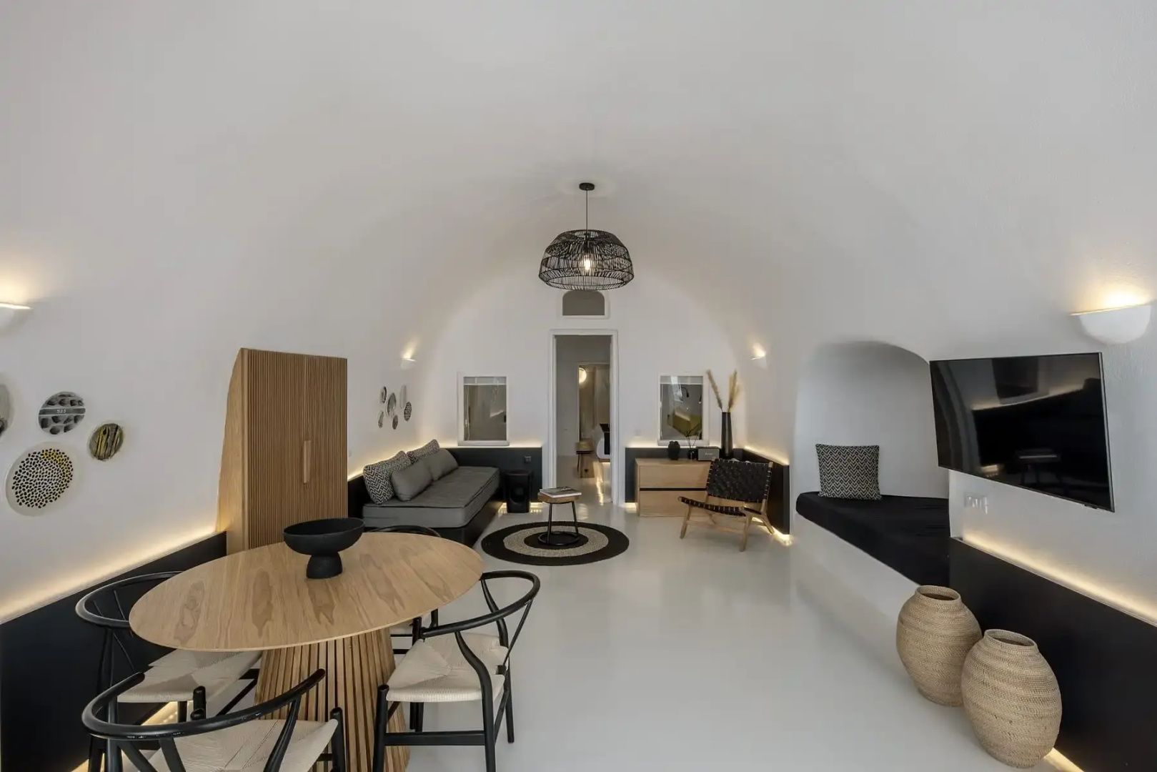 Heller Wohnbereich im Höhlendesign mit rundem Esstisch, grauem Sofa und Einbausitzbank.