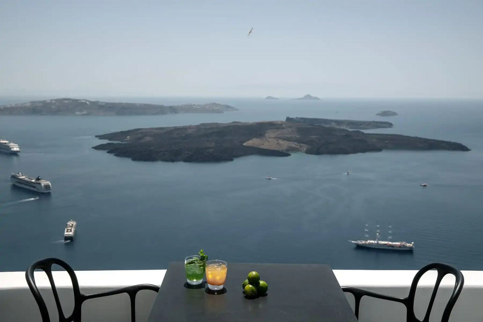 Tisch auf einer Terrasse mit zwei Gläsern und Blick auf die Ägäis sowie Vulkaninseln.