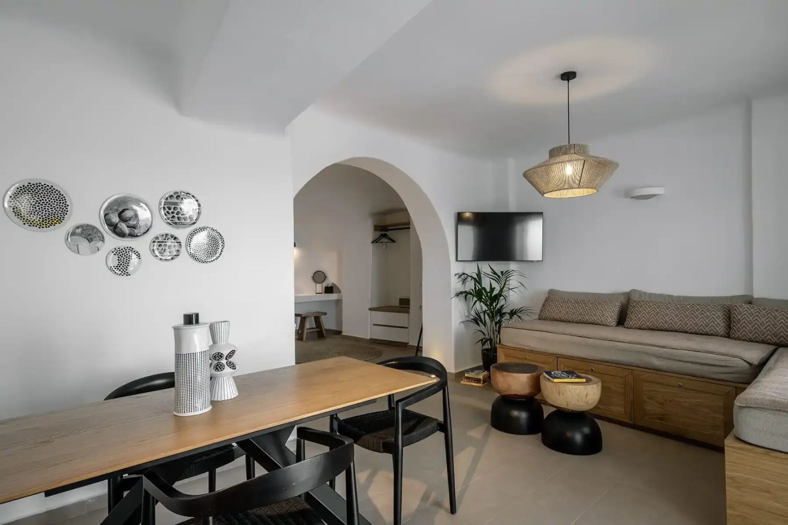 Wohnbereich einer Suite mit Holztisch, schwarzem Stuhl, Sofa und Rundbogen zum Nebenraum.