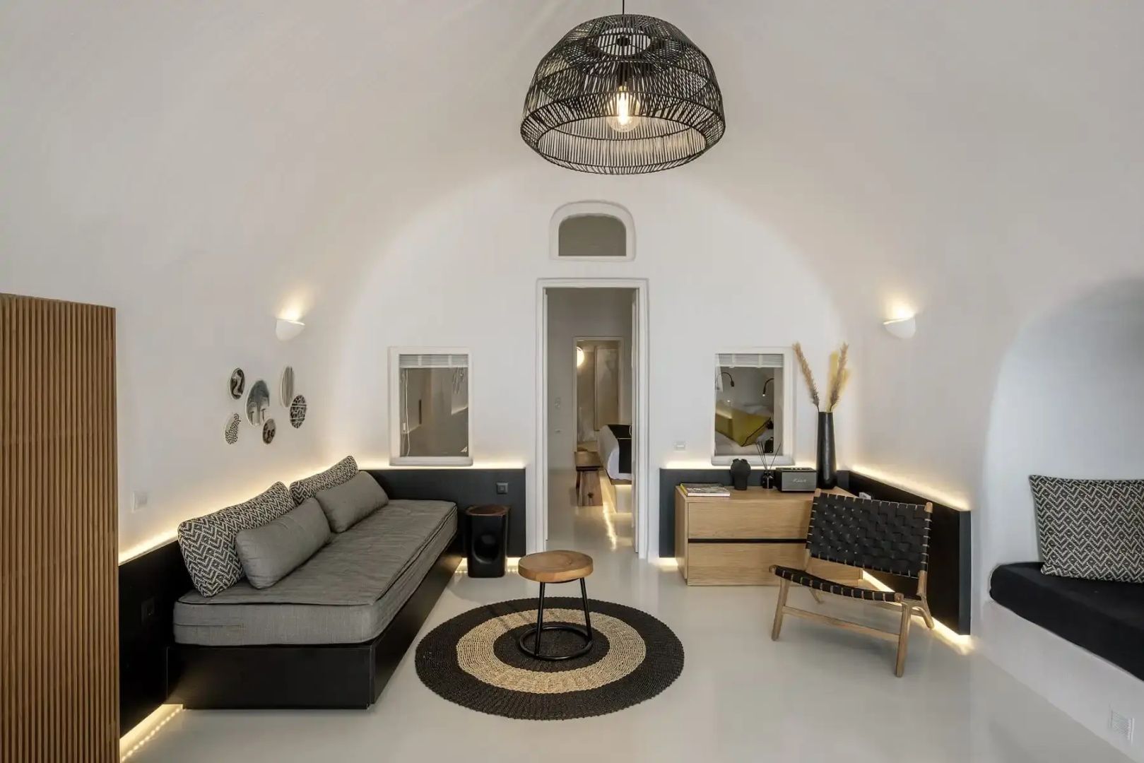 Wohnbereich mit gewölbter Decke, grauem Sofa, rundem Teppich und Holzmöbeln.