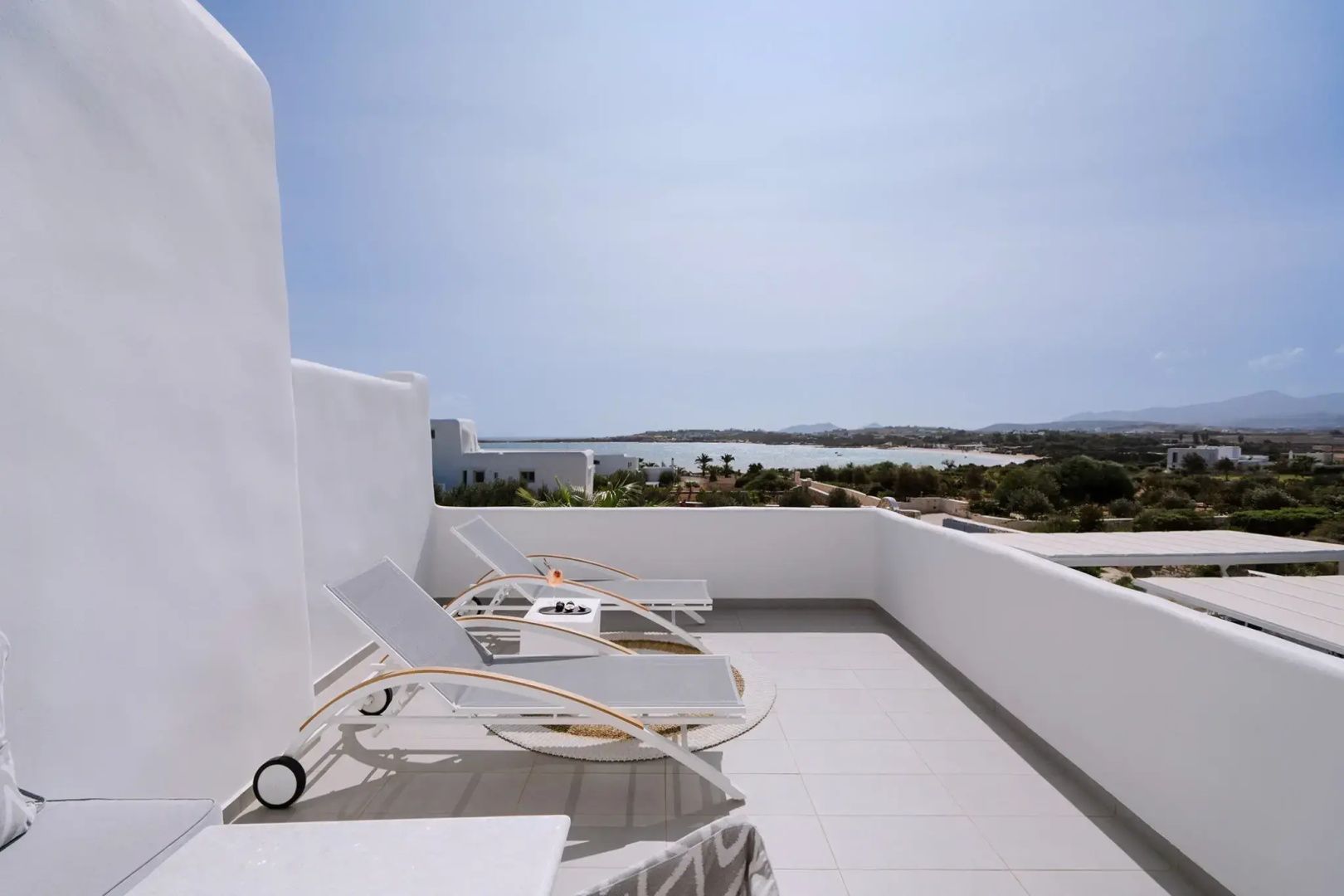 Sonnige Terrasse mit zwei Liegestühlen und freiem Blick auf die Küstenlandschaft und das Meer.