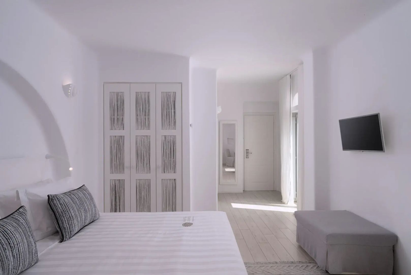 Weiß gestaltetes Hotelzimmer mit großem Bett, Einbauschrank und hellem Holzboden.