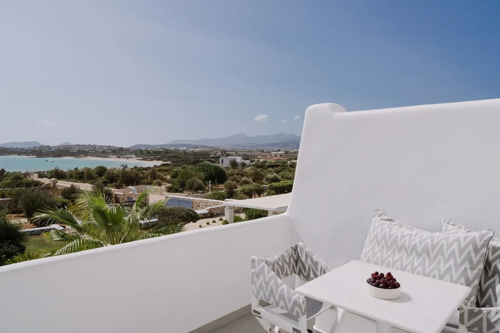 Weißer Balkon mit Stühlen und Blick über die grüne Küstenlandschaft bis zum Meer.