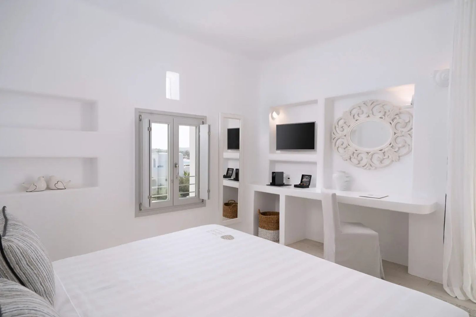 Weiß gestaltetes Zimmer mit Bett, weißem Schreibtisch, TV in der Wandnische und Fenster