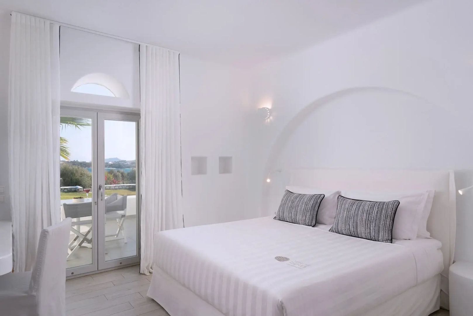Helles Hotelzimmer mit Doppelbett, weißer Bettwäsche und Zugang zur Terrasse.