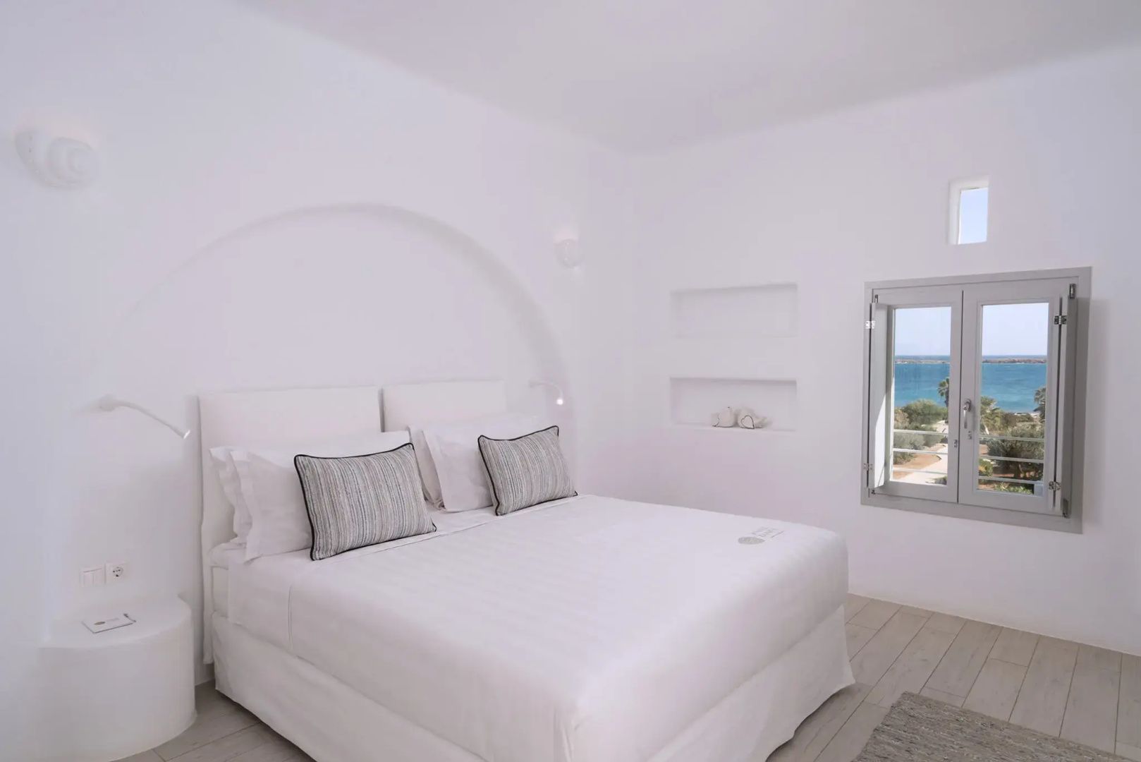 Doppelbett in weiß gehaltenem Zimmer mit Rundbogen und Ausblick auf das Meer
