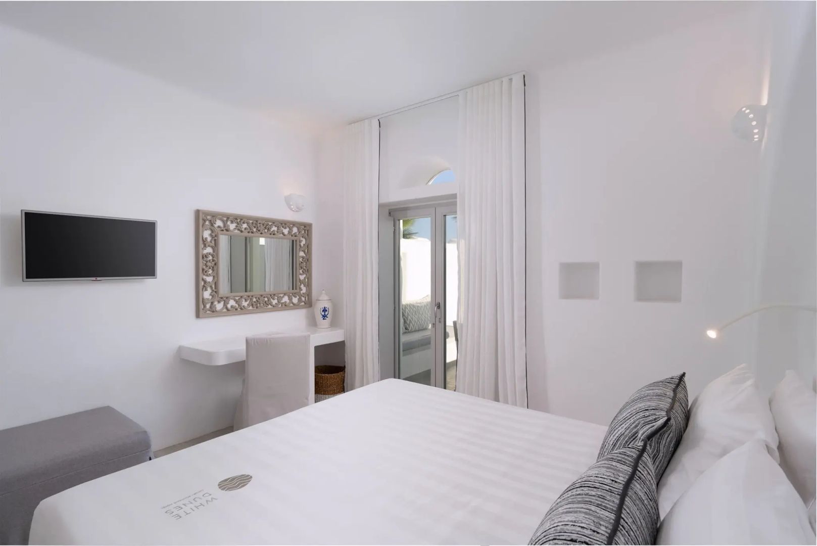 Weiß eingerichtetes Schlafzimmer mit Schminktisch, Wandspiegel und Glastür.