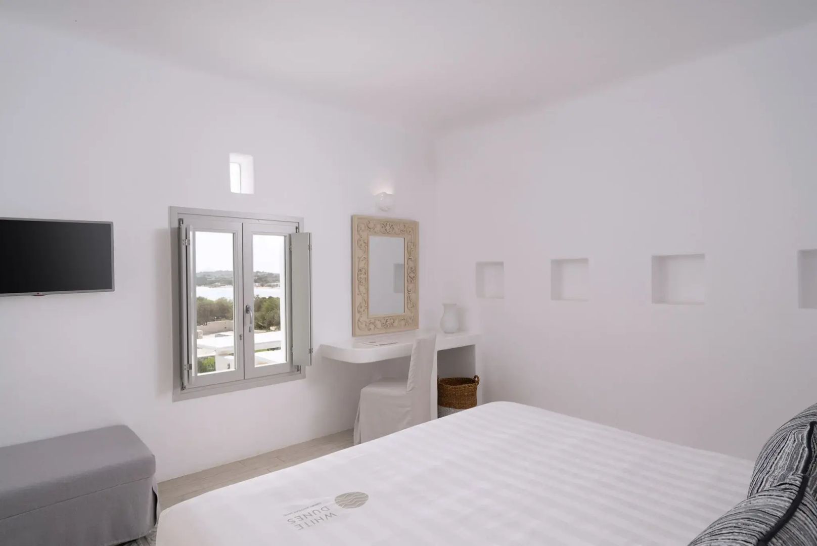 Weißes Schlafzimmer mit Schminktisch, Wandspiegel und Blick aus dem kleinen Fenster.