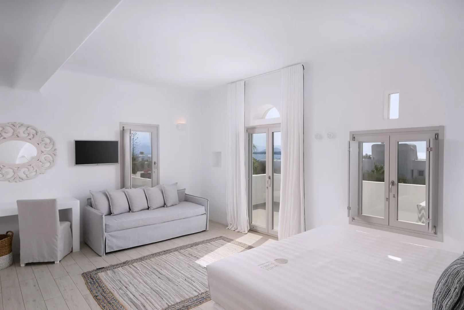 Weißes Zimmer mit einem Sofa, Fernseher an der Wand und Zugang zum Balkon.