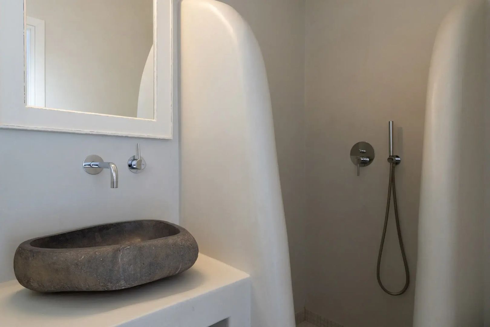 Badezimmer mit grauem Steinwaschbecken, Wandarmatur und Duschbereich.