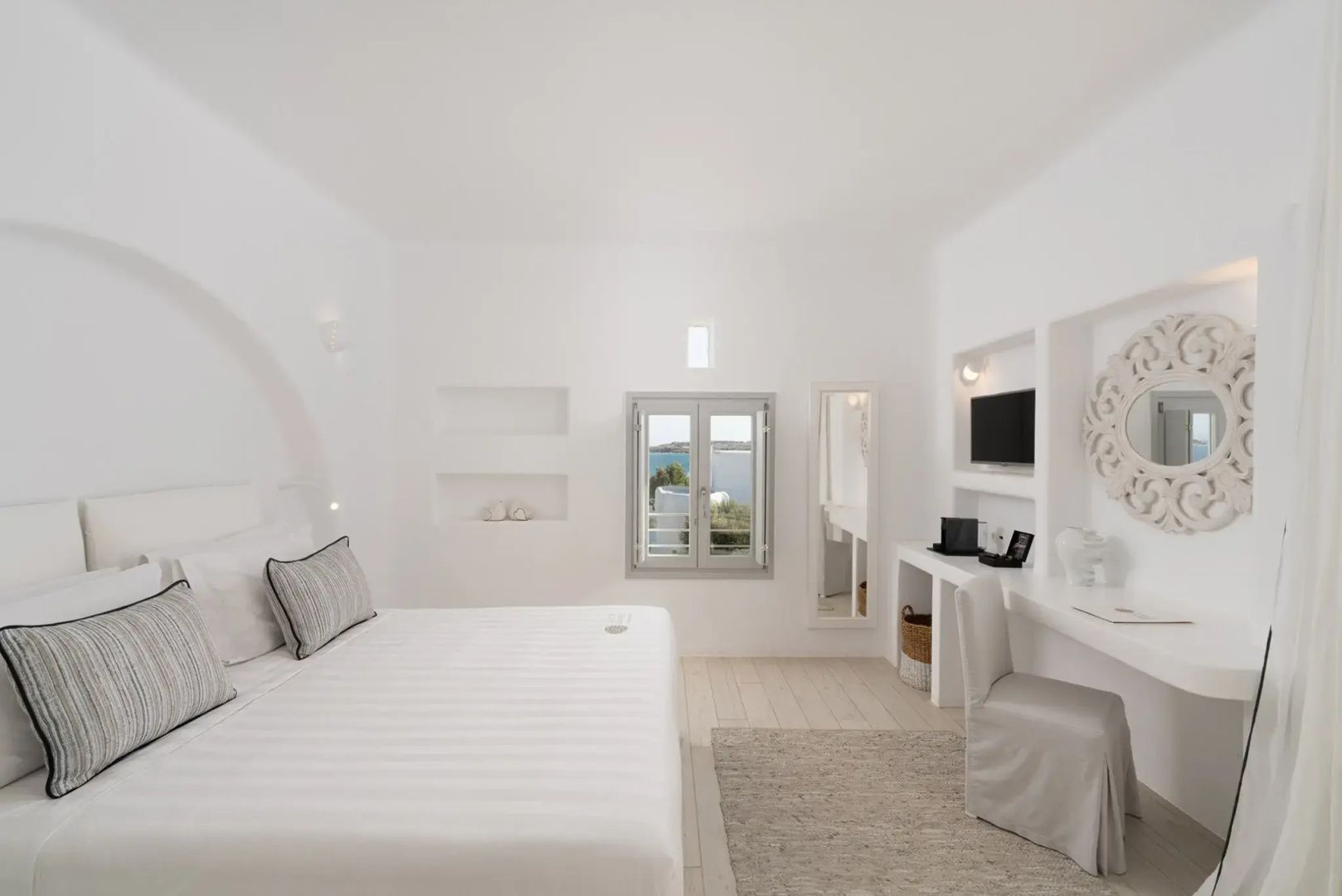 Geräumiges weißes Schlafzimmer mit Doppelbett, Schreibtisch, Fernseher und Meerblick