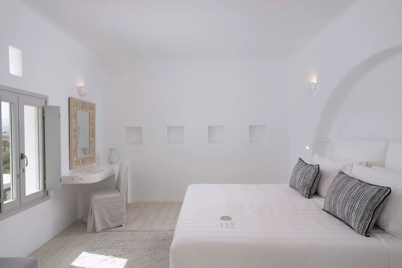 Doppelbett mit weißer Bettwäsche, Wandnischen und Schminktisch im hellen Zimmer.