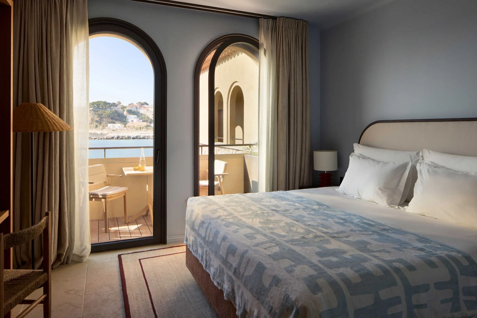 Hotelzimmer mit Doppelbett und rundbogigem Zugang zum Balkon mit Meerblick.
