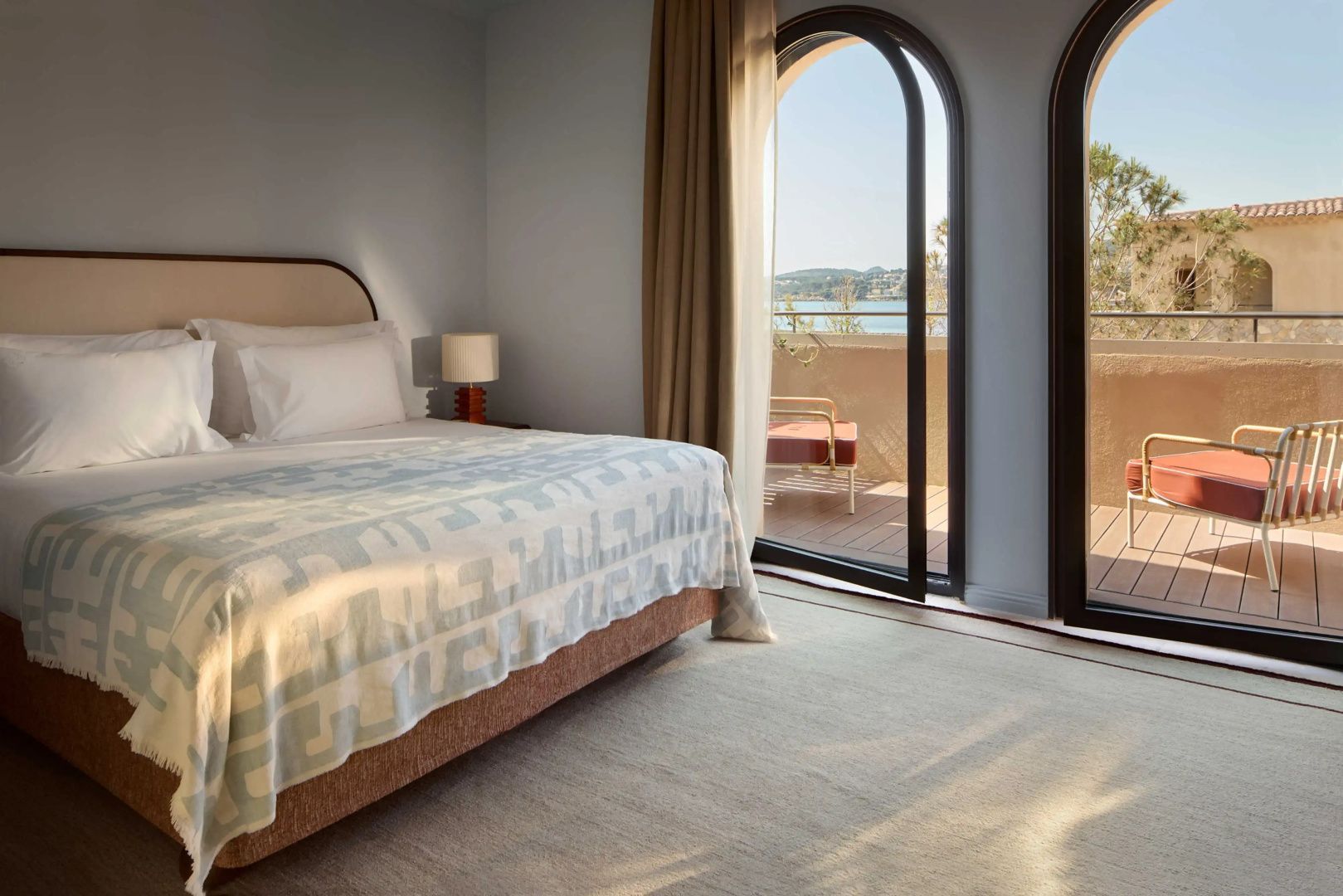 Schlafzimmer mit Doppelbett und hohen Rundbogentüren mit Blick auf das Meer.