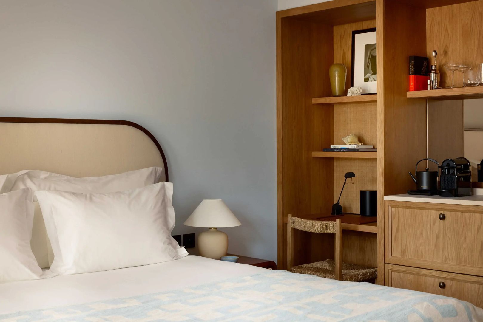 Hotelzimmer mit gepolstertem Kopfteil, Nachttischlampe und Nische mit Schreibtisch.