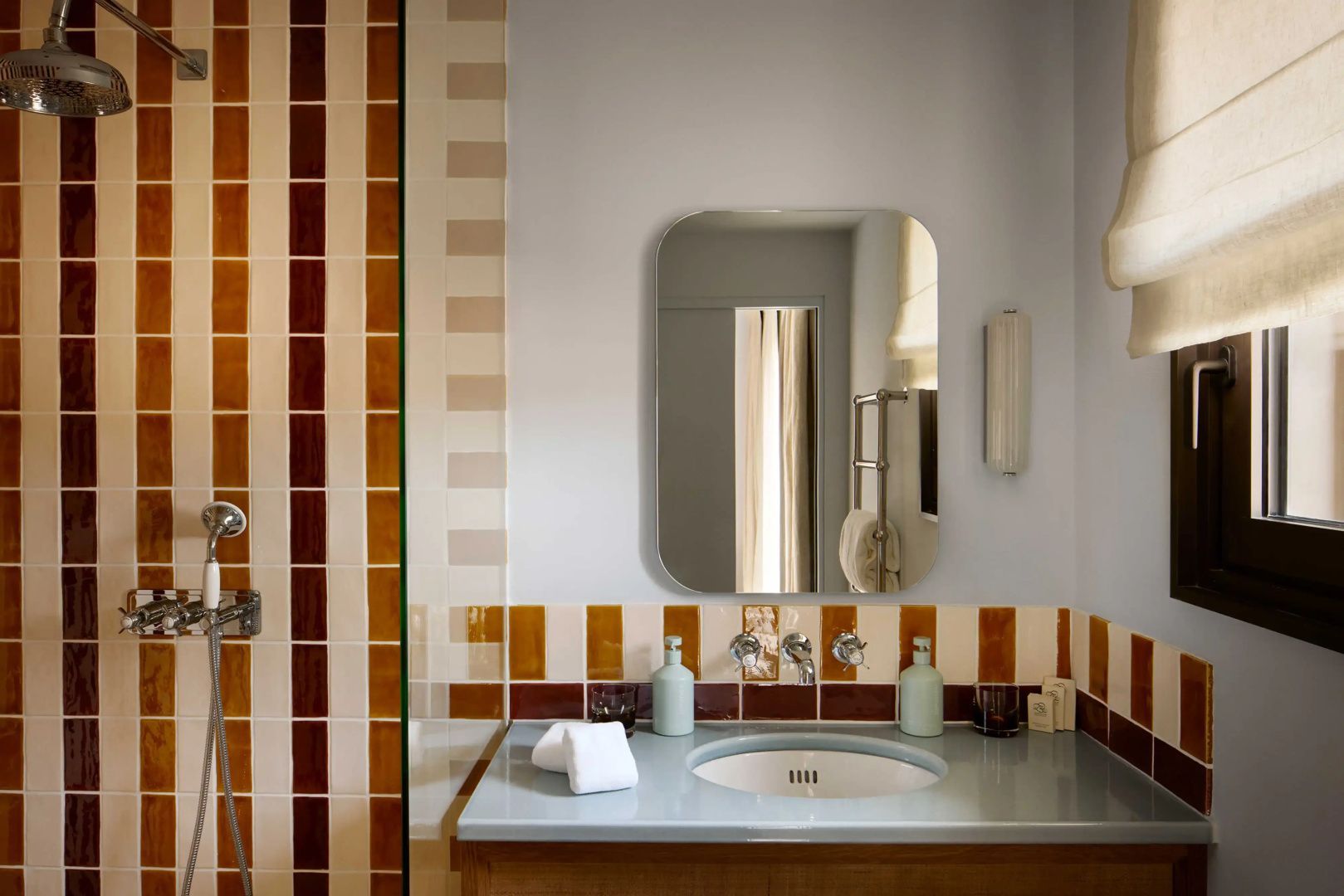 Waschtisch mit ovalem Wandspiegel, blauem Countertop und gestreiften Wandfliesen im Badezimmer.