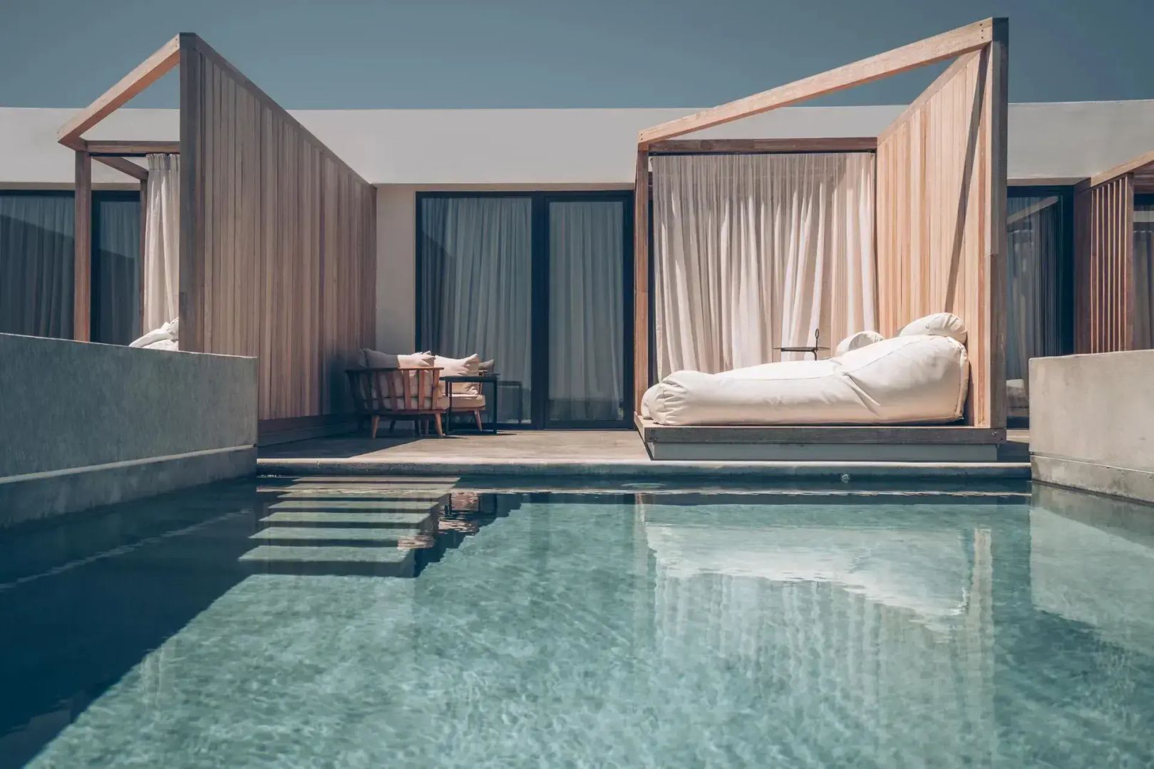 Terrasse mit privatem Pool, gepolsterter Liege unter einer Holzkonstruktion und Holzwand.