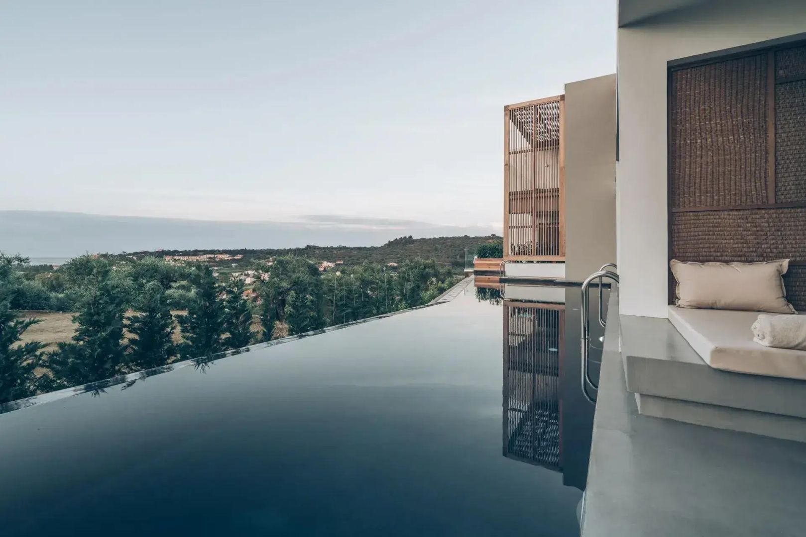 Infinitypool am Hotelgebäude mit weitem Blick über Bäume und die hügelige Landschaft.