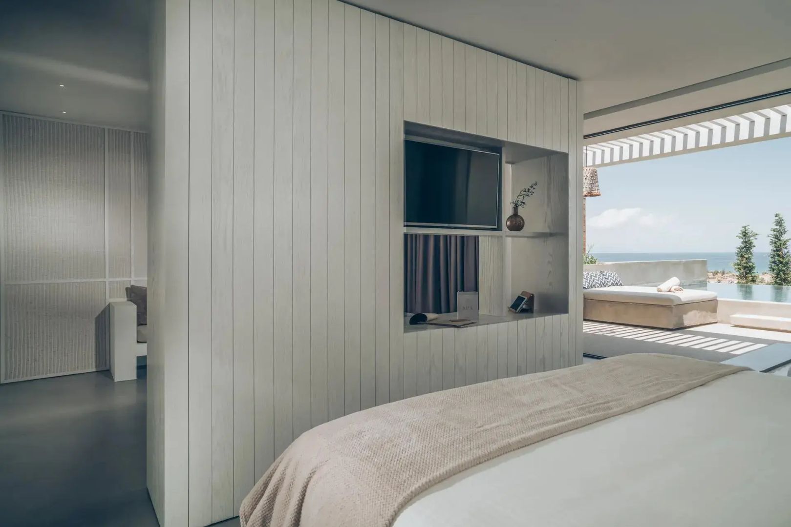 Helles Hotelzimmer mit weißer Holzwand, Fernseher im Wandregal und Blick auf die Terrasse.