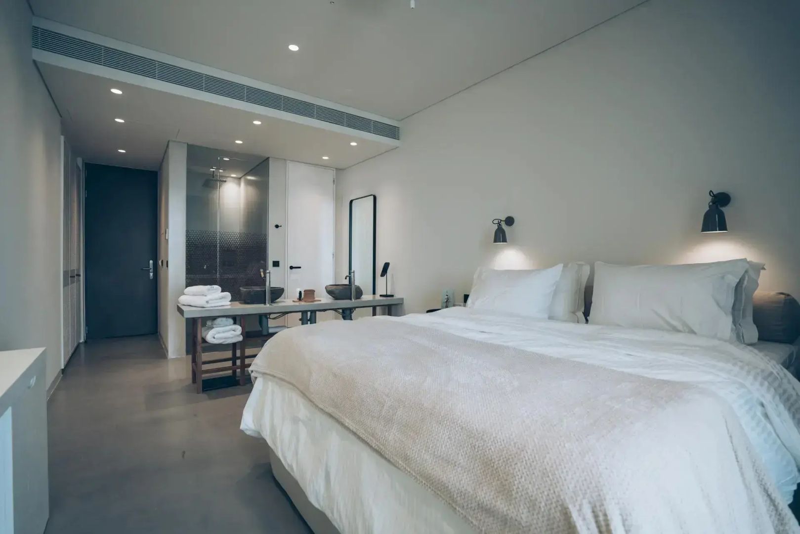 Helles Hotelzimmer mit großem Doppelbett und offen gestaltetem Badezimmer im Hintergrund.