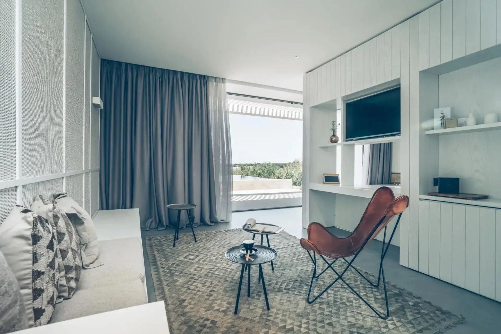 Wohnbereich der Suite mit braunem Ledersessel, Teppich, Sofa und Ausblick ins Grüne.