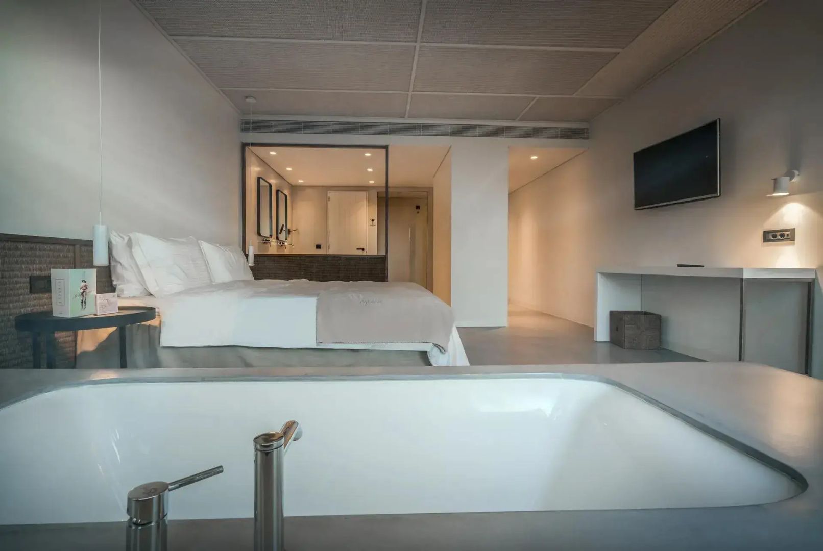 Blick über die Badewanne auf das Doppelbett und den TV-Bereich der hellen Suite.
